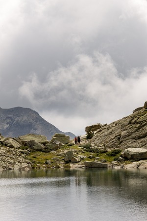 A couple of hikers walk near a lake on a stormy day.の写真素材
