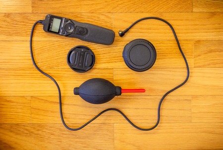 A wooden background with a set of photography accessories consisting of a lens cap, a...