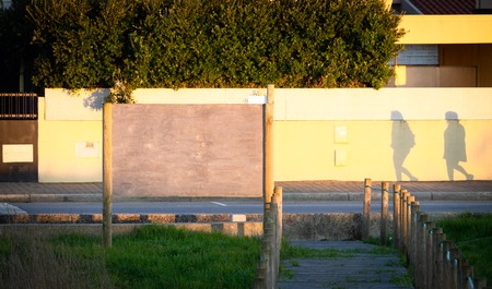 Wooden advertisement billboard mockup near the shadows of two people. Warm light. Copy Space.