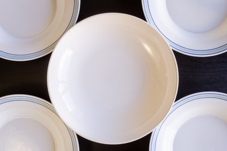 A black wooden background with five blue and white empty plates.