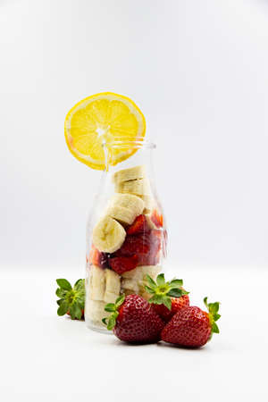Fruit salad consisting of bananas and strawberry inside a glasse bottle, with three straberrries and...