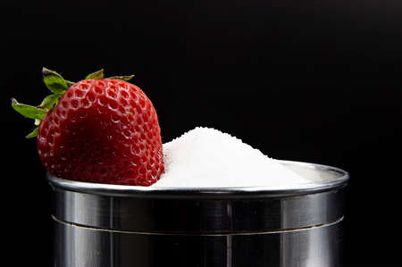 A strawberry lyng on top of a mound of sugar in a silvery jar on a dark backgroundの写真素材