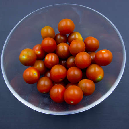 Photograph of a glass salad bowl and cherry tomatoes on a dark backgroundの写真素材