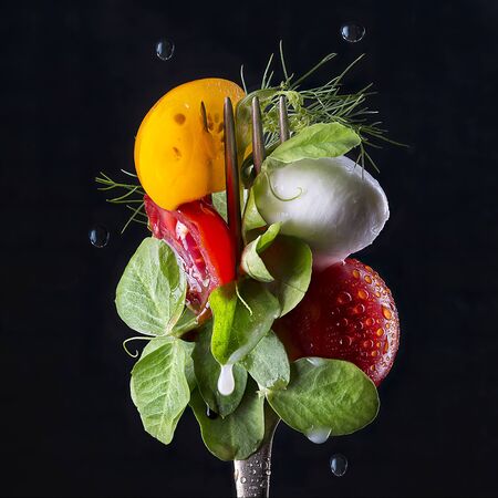 Macro view of fresh salad, lettuce and tomato on the fork; isolated on black background.