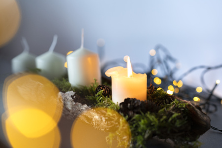 closeup of an advent christmas wreath line with 4 candels the first candel is burning, christmas light stripes in a blurred out backgroundの写真素材