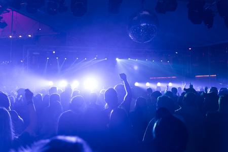 a crowd of people partying in a disco club, light and lasers and foggy environment, a man putting his hand up in the airの写真素材