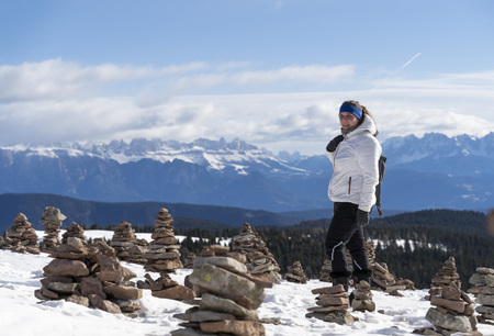 beautiful landcape view of the stoanerne mandln with the dolomites in the background in South Tyrol, sarntal, jenesien during winter with a girl standing in the middle and is enjoying the sunの写真素材