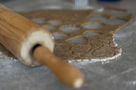 close up of a rolling pin and a biscuit dough with cutted out cookies on a kitchen table