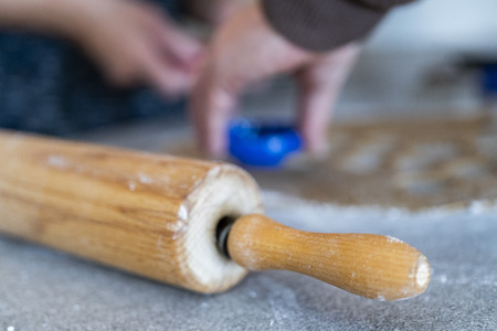 close up of a rolling pin and hands who are cutting out cookies of the biscuit dough in a kitchenの写真素材