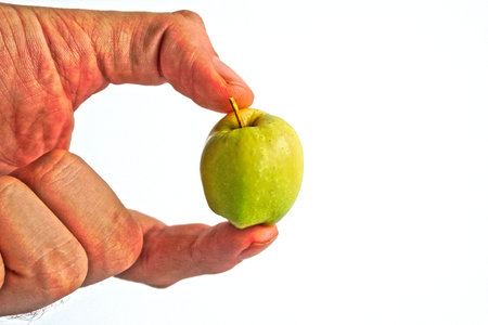 Male hand holding a tiny green apple on a white backgroundの写真素材