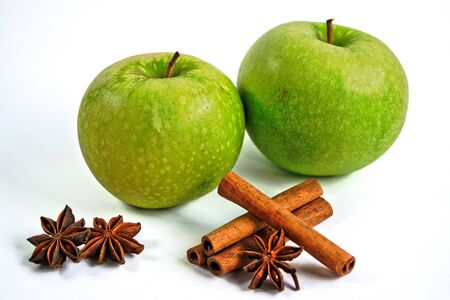 Two green apples with cinnamon sticks and star anise on a white backgroundの写真素材