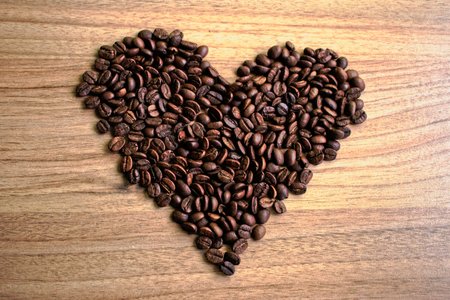 Coffee beans in a heart shape on a wooden tableの写真素材