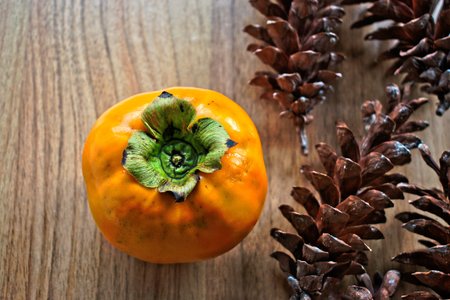 Persimmon and pine cones on a wooden tableの写真素材
