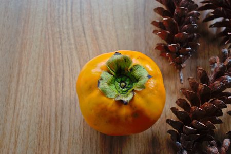 Persimmon and pine cones on a wooden tableの写真素材