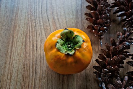 Persimmon and pine cones on a wooden tableの写真素材