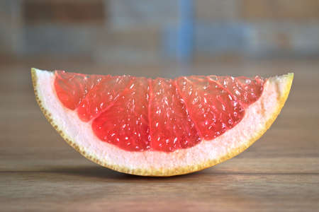 Closeup of a red grapefruit wedge on a wooden tableの写真素材