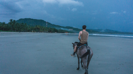 Man in tanktop riding a horse in the dusk at the beachの写真素材
