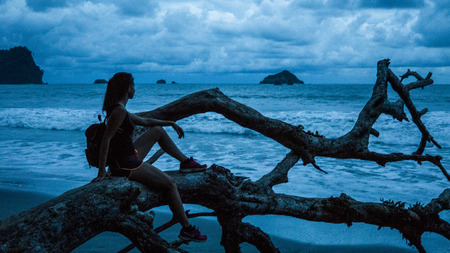 Silhouette of Woman enjoying the beach at dusk on a fallen treeの写真素材