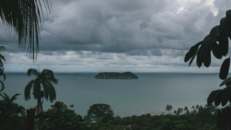 Small island on the sea seen through the jungle at a dark cloudy dayの写真素材