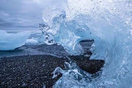 Closeup of a beached iceberg in the shape of a frozen wave during midnight sun on a cloudy night at...