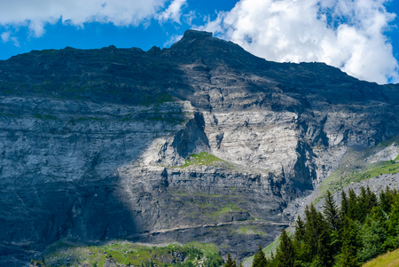 Plain-Joux, France: Mountain ridge rich in contrast due to shadow and sunlight in with pine trees in the right corner. Above the ridge is a blue sky with white clouds.の写真素材