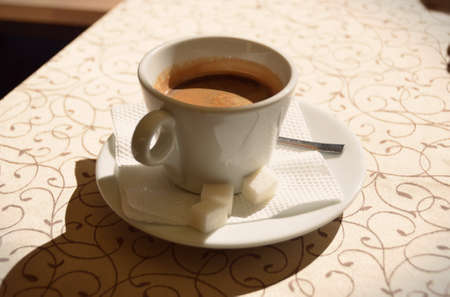 cup of hot coffee on a saucer with sugar stands on a patterned tablecloth vintageの写真素材