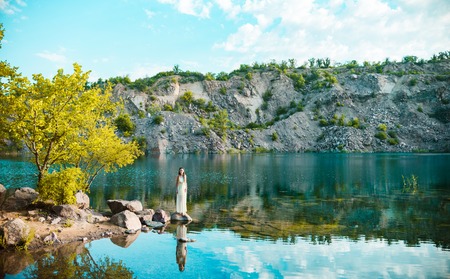 A beautiful girl in a white dress with dreadlocks is standing on the lake. Lake at sunrise
