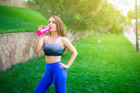 Fit young woman drinking water after training, big city is in the background