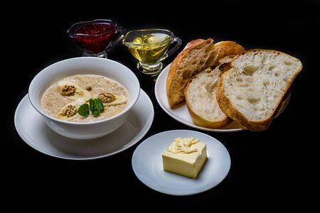 Oatmeal in a white plate with banana and mint. next to a plate of bread, butter, honey and jam on a black background. Healthy breakfast.の写真素材