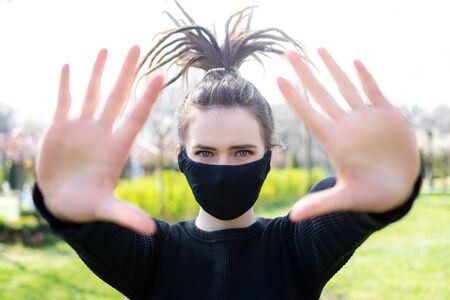 A girl in a protective mask with collected dreadlocks up holds her hands in front of her.の写真素材