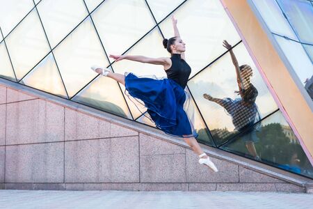 beautiful young woman dancer in the city dressed in dance clothes is dancing on the move and jumpingの写真素材