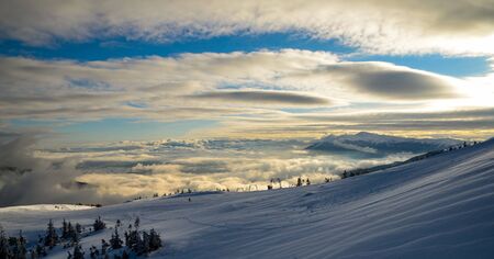 Aerial view above the clouds at mountain peaks covered with snow, lighting by the sunの写真素材