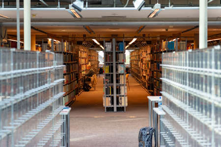 February 18, 2019. Warsaw, Poland. University Library. Bookshelf in library with many books. Interiour of the famous public library. In the distance, an elderly professor sits and reads booksのeditorial素材