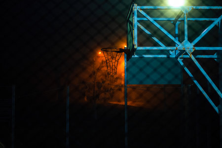 Empty basketball court at night. View through the grid. The light of lanterns in the fog.の写真素材