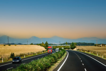 Autobahn with cars on the road. Road among agricultural fields with mountains on the horizon during...