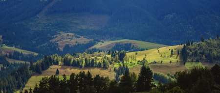Wonderful mountain land with forest and small houses in sunlight. Scenic view to vast expanses of rolling hills and great mountain ridge on horizon. Immense distances of wavy relief in evening light.の写真素材