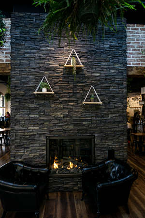 Interior of a cafe or a restaurant with stone brick wall and hanging plants. Fireplace in a wall with two armchairsの写真素材
