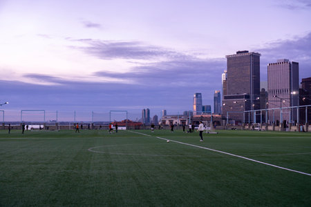 New York City, USA - December 18, 2021: Pier 5 soccer field in Brooklyn. Turf field with people playing soccer at sunset with view of tall modern buildingsのeditorial素材