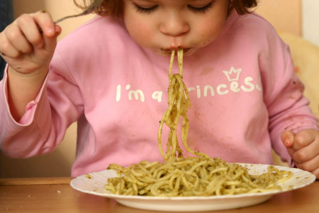 little child eating pasta with pesto sauceの写真素材