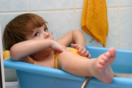 little child having a bath in small blue bathtub