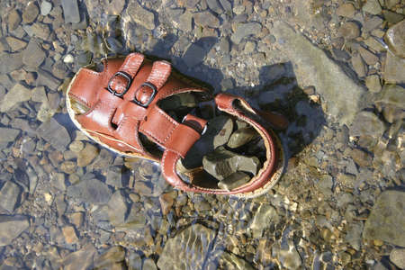 Kid's shoe left in water full of stones.の写真素材