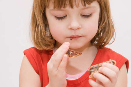 little, cute girl eating cakes isolated on whiteの写真素材