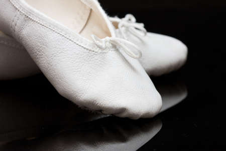 white child's ballet slippers on black, reflecting backgroundの写真素材