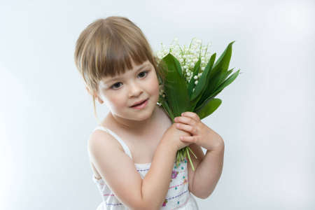 little, pretty girl holding bunch of lilies of the valley on white backgroundの写真素材