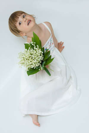 little, pretty girl holding bunch of lilies of the valley on white backgroundの写真素材
