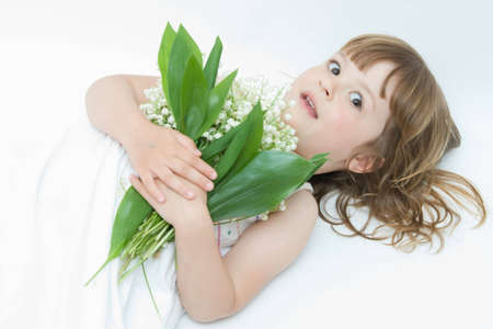 little, pretty girl holding bunch of lilies of the valley on white backgroundの写真素材