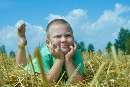 happy boy resting on a stubble fieldの写真素材