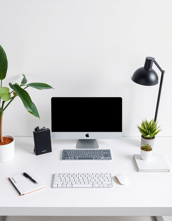 Minimal workspace with computer, keyboard, notebook and plant on white table.の写真素材