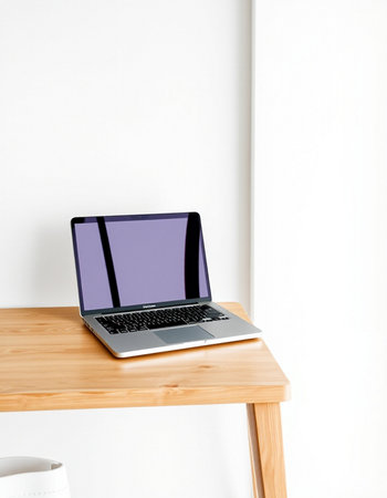 Laptop on a wooden table in front of a white wall.
