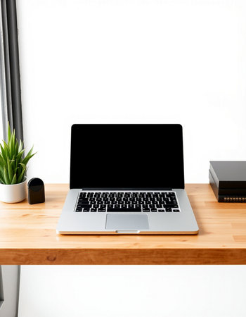 Laptop with blank screen on wooden table and white wall background.